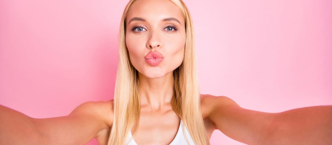 Photo of amazing lady making selfies for beauty blog sending air kiss to followers wear white tank-top isolated pink color background