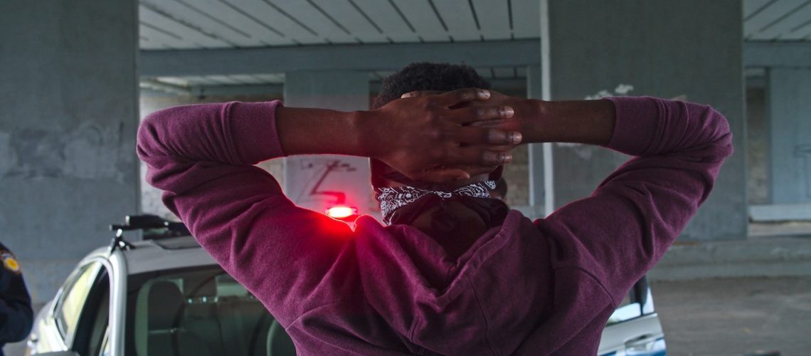 Close-up black offender in mask caught red-handed by the police. Two old friends afro-american men cop and thief meeting at arrest. Amazing fun scene. Police on duty.