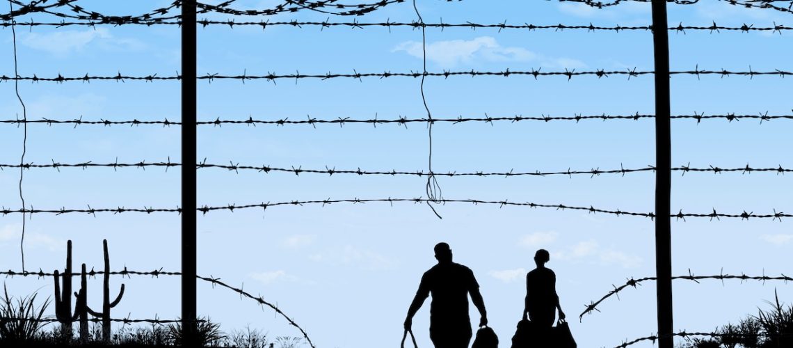 A man and woman are seen in silhouette after breaching a border fence on the southern border of the USA. They have gone through a broken barbed wire fence.