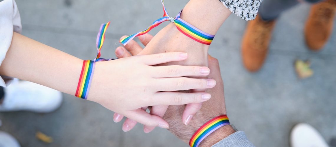 Hands of a group of three people with LGBT flag bracelets. LGBT pride celebration.