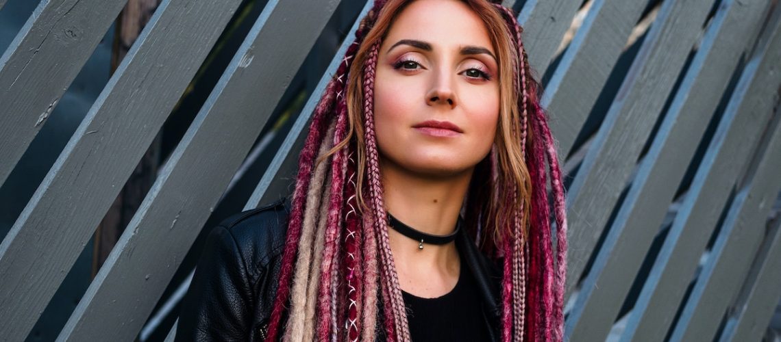 portrait of an attractive young woman in black clothes with pink de-dreadlocks on a gray wall background with wooden planks