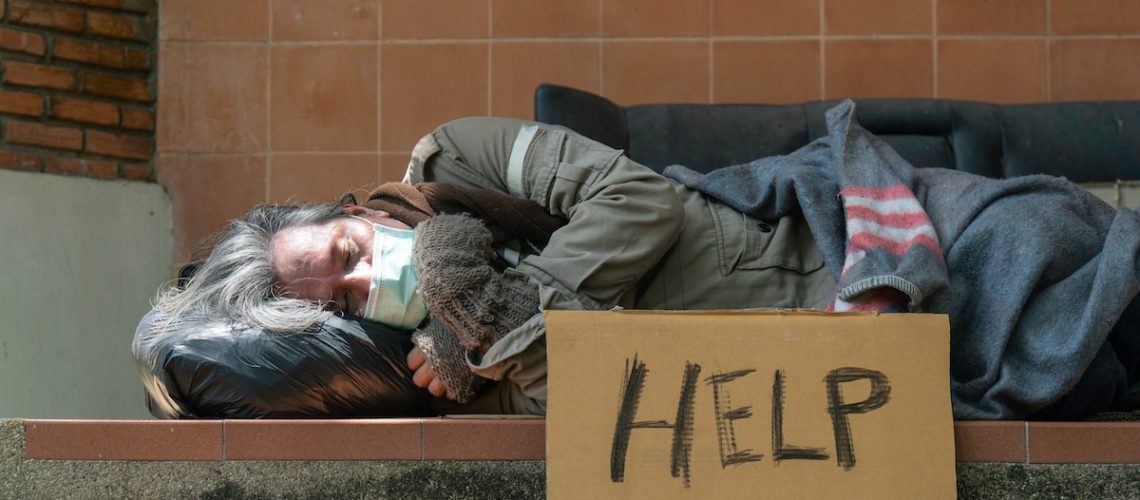 A homeless man sleeps on the side of the road.