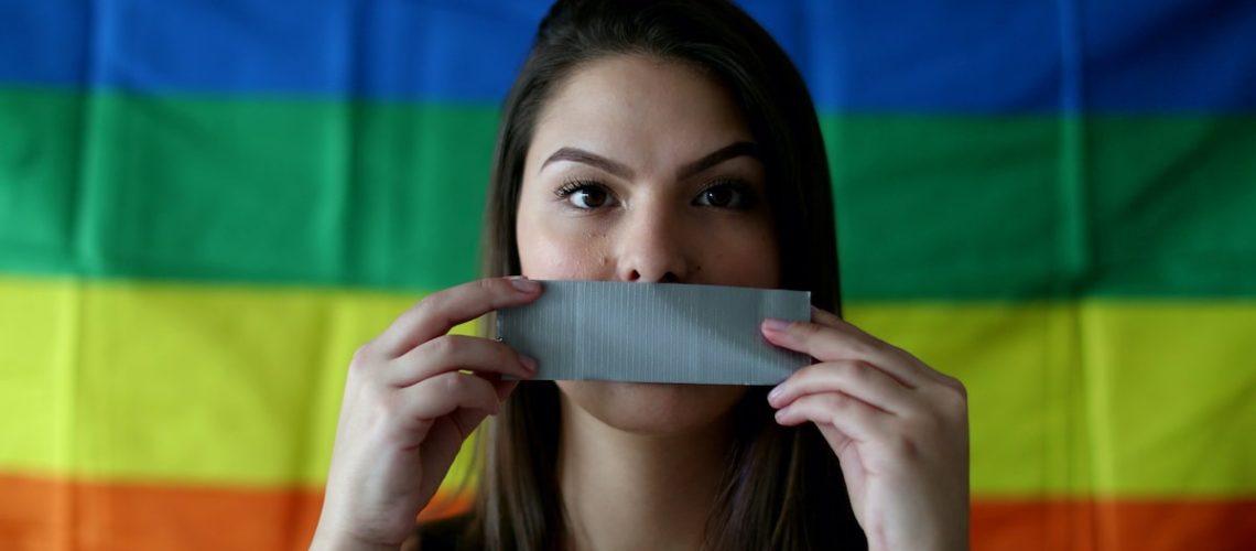 Young woman covering mouth with duct tape. LGBT censorship concept